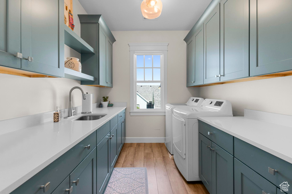 Laundry room featuring washer and dryer, cabinet space, baseboards, and light wood-style flooring