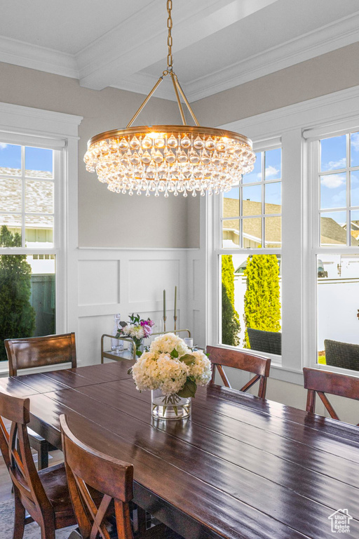 Dining area featuring a chandelier, crown molding, a decorative wall, and wainscoting