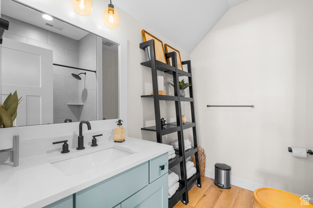 Full bathroom featuring wood finished floors, a tile shower, vanity, lofted ceiling, and baseboards
