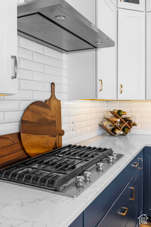 Kitchen with exhaust hood, stainless steel gas stovetop, blue cabinets, and white cabinets