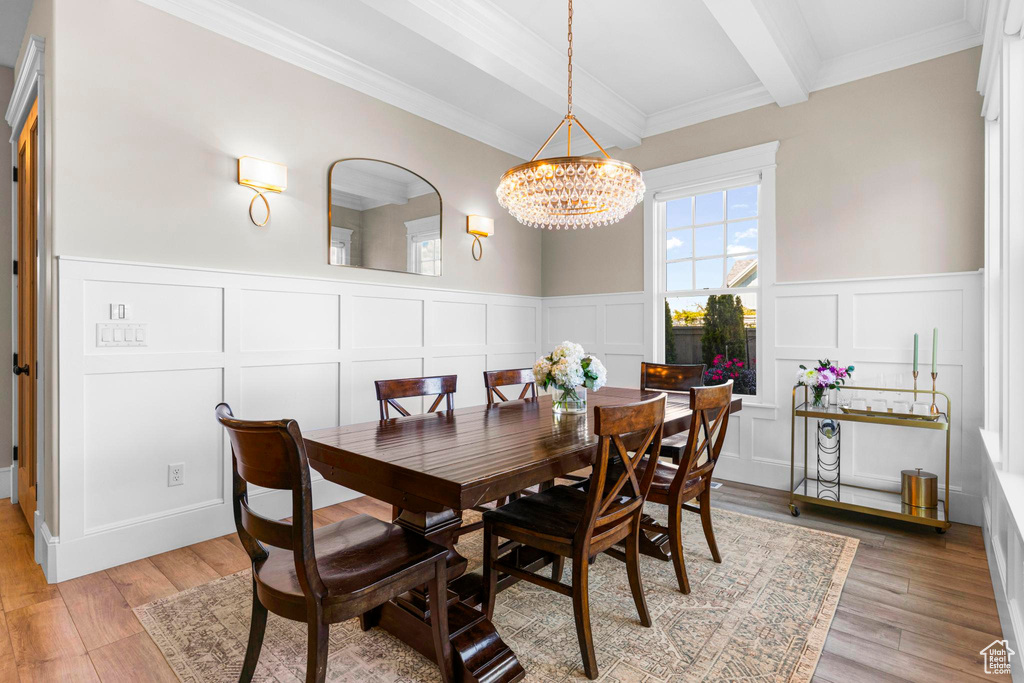 Dining room with a decorative wall, beam ceiling, a chandelier, light wood-style floors, and ornamental molding
