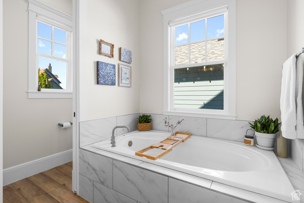Bathroom with plenty of natural light, baseboards, wood finished floors, and a bath