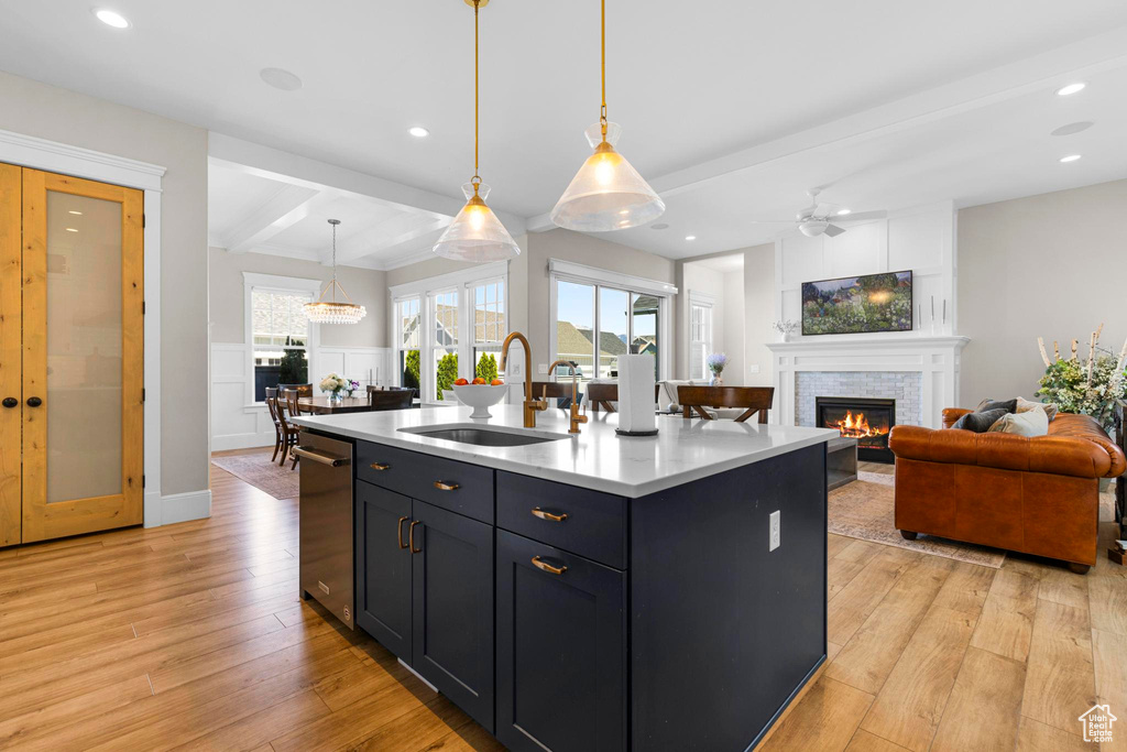 Kitchen featuring a sink, open floor plan, a glass covered fireplace, light wood-style floors, and beamed ceiling