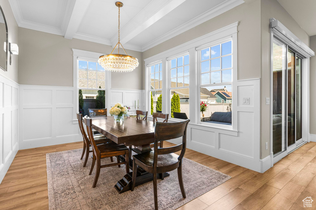 Dining room featuring a decorative wall, a chandelier, light wood finished floors, beam ceiling, and a wainscoted wall