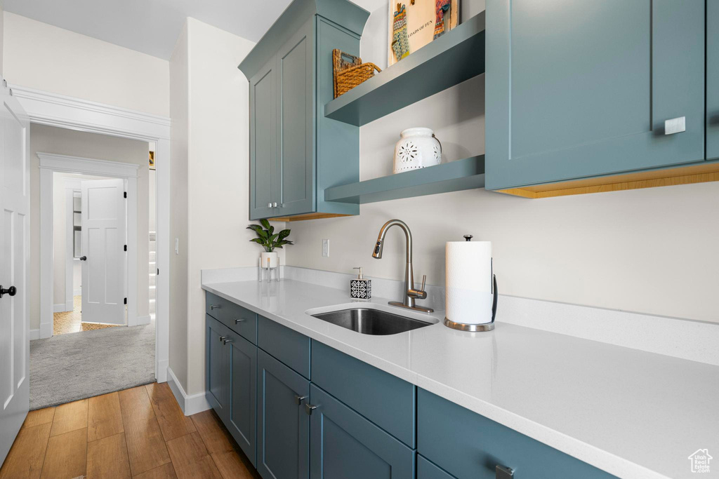Kitchen with a sink, open shelves, wood finished floors, light countertops, and baseboards