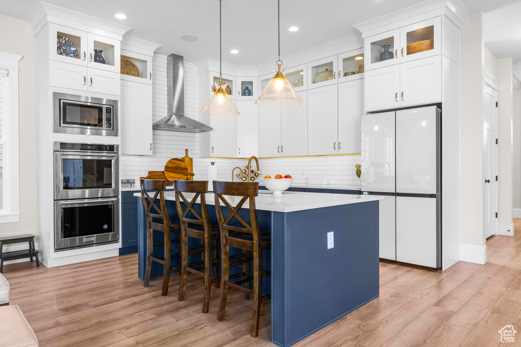 Kitchen with stainless steel appliances, wall chimney range hood, light wood-style flooring, light countertops, and recessed lighting