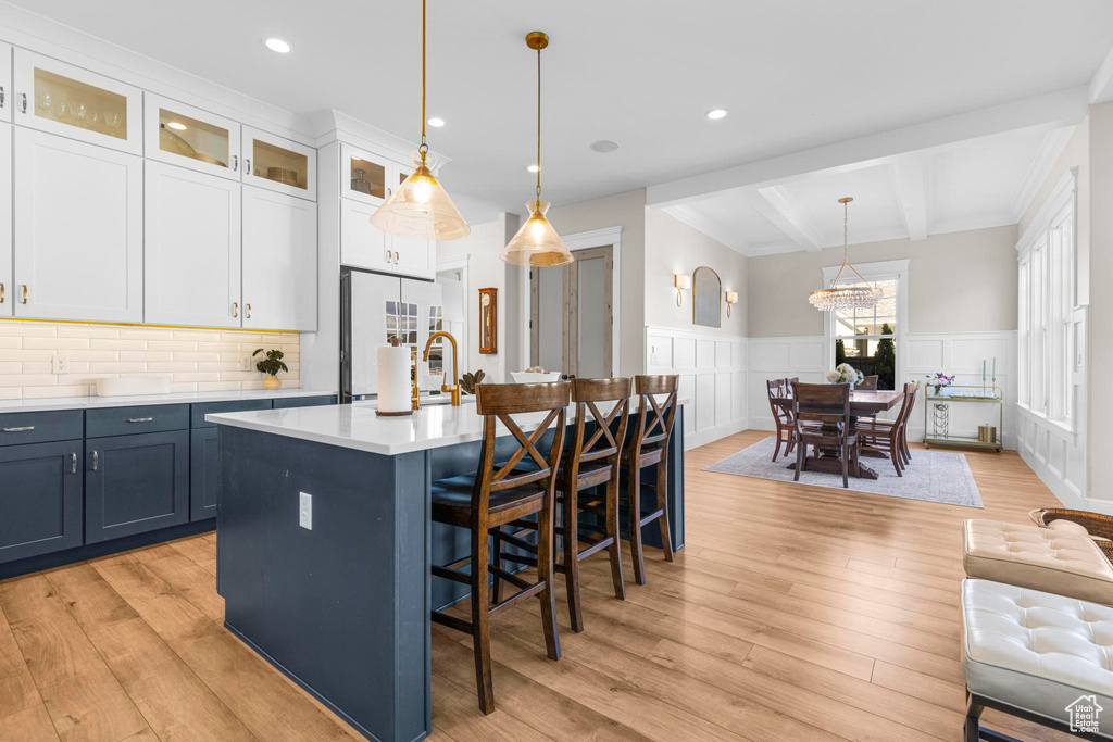 Kitchen featuring white refrigerator, beamed ceiling, light countertops, light wood-style floors, and a kitchen breakfast bar