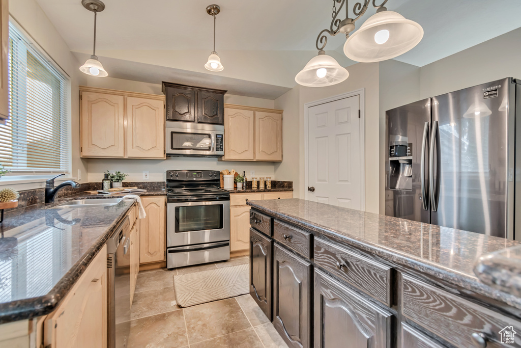 Kitchen featuring appliances with stainless steel finishes, a sink, light brown cabinets, vaulted ceiling, and pendant lighting