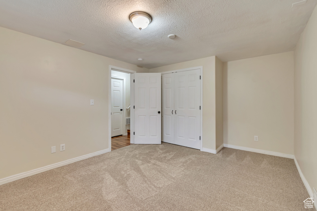 Unfurnished bedroom with carpet flooring, a textured ceiling, baseboards, and a closet