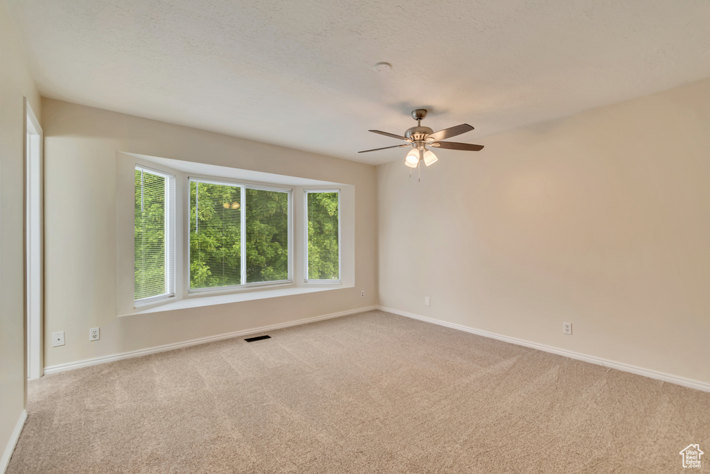 Empty room featuring carpet flooring, baseboards, and a ceiling fan
