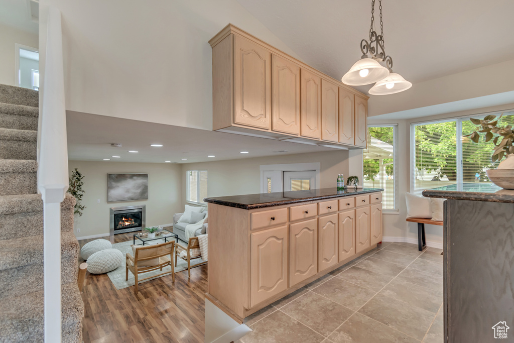 Kitchen with light brown cabinets, a glass covered fireplace, dark stone counters, recessed lighting, and pendant lighting