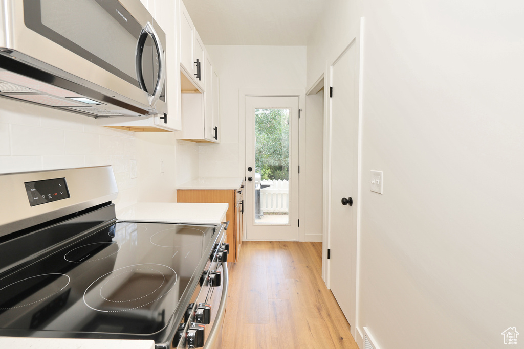 Kitchen with stainless steel appliances, light wood-type flooring, white cabinetry, and light countertops