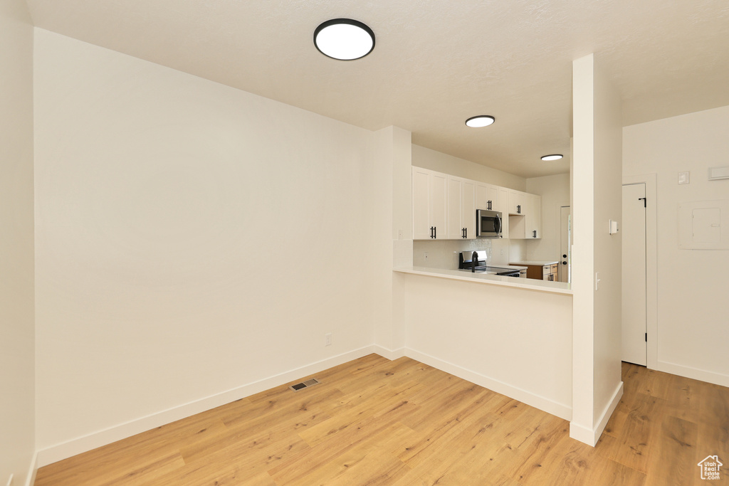 Kitchen with stainless steel appliances, light wood-style flooring, light countertops, baseboards, and white cabinets