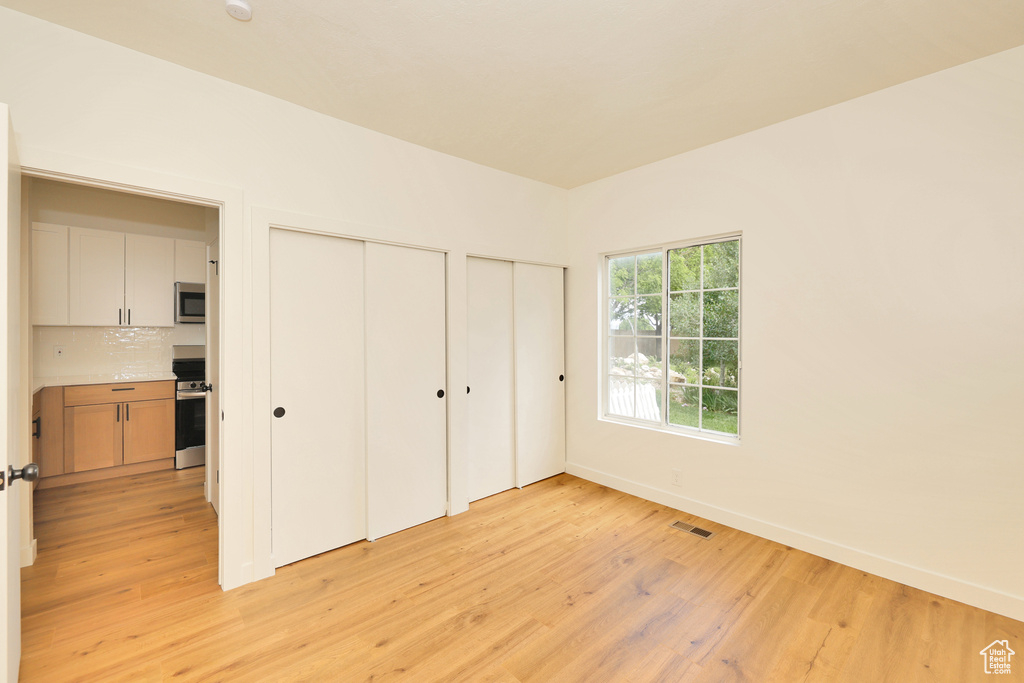 Unfurnished bedroom featuring two closets, light wood-style flooring, and baseboards