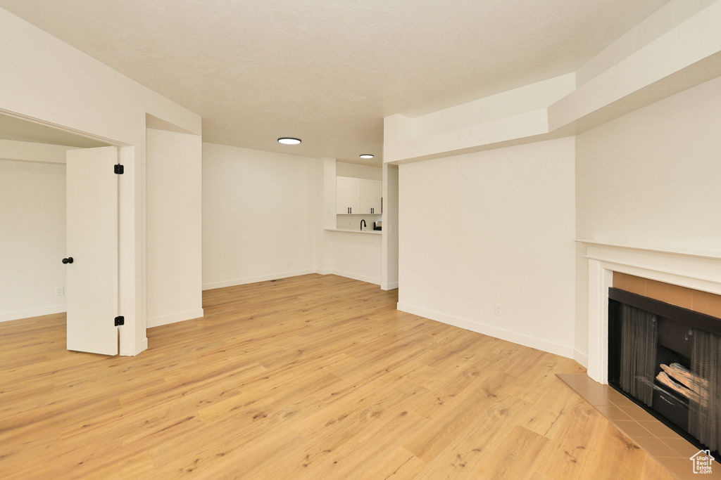 Unfurnished living room featuring a tiled fireplace, light wood-type flooring, baseboards, and recessed lighting