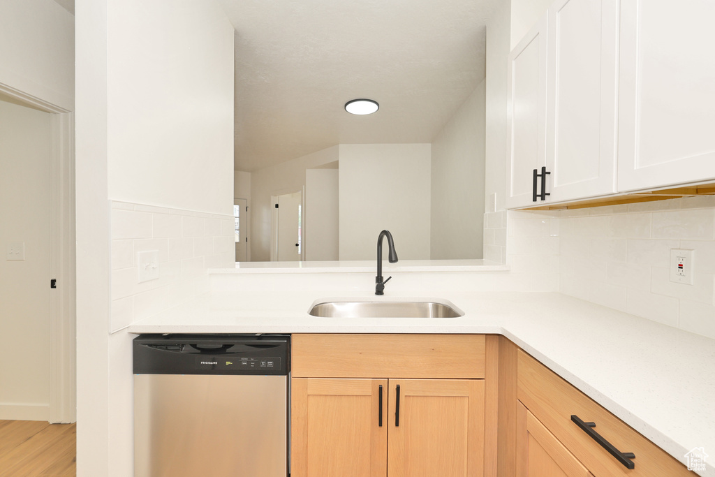 Kitchen with dishwasher, a sink, light countertops, and backsplash