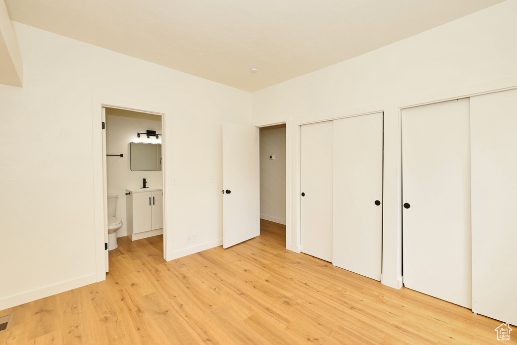 Unfurnished bedroom featuring two closets, light wood finished floors, ensuite bath, baseboards, and a sink