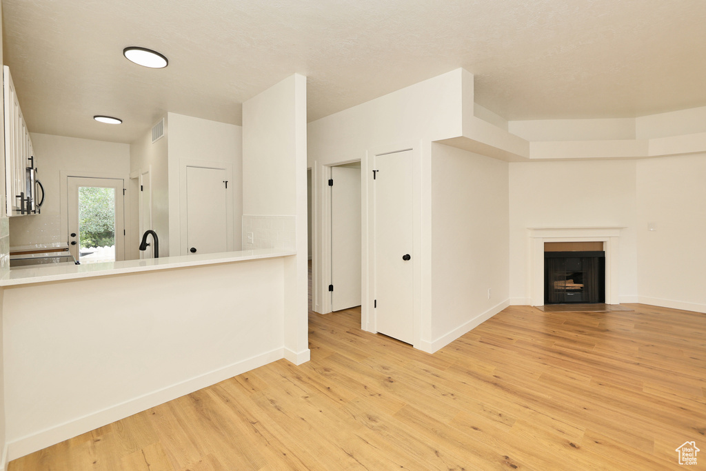 Unfurnished living room with light wood finished floors, baseboards, and a fireplace with flush hearth