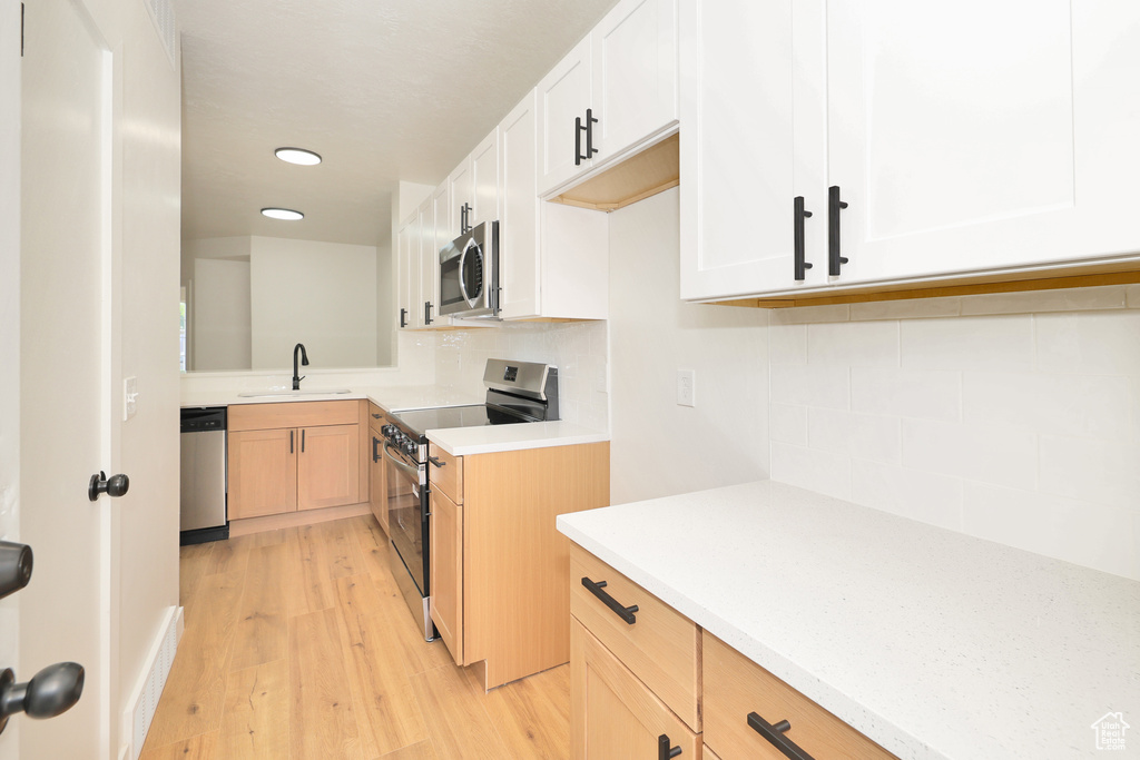 Kitchen featuring stainless steel appliances, a sink, light countertops, tasteful backsplash, and light wood-type flooring