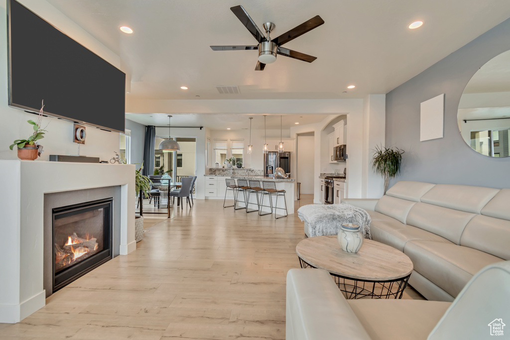 Living room with ceiling fan, light wood-style flooring, recessed lighting, and a glass covered fireplace