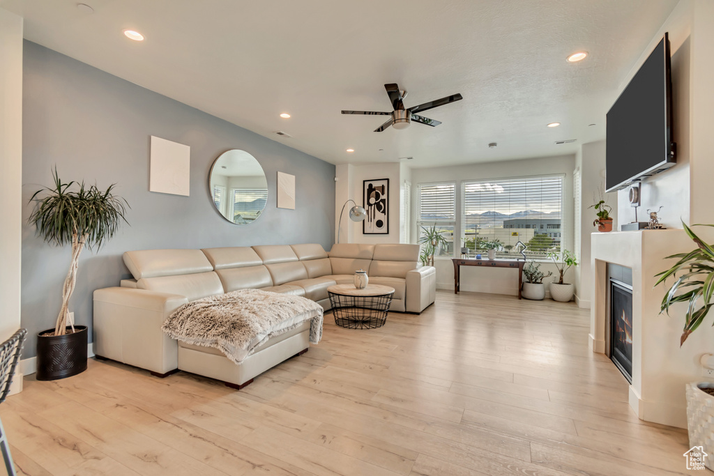 Living room with ceiling fan, recessed lighting, light wood-style flooring, and a glass covered fireplace