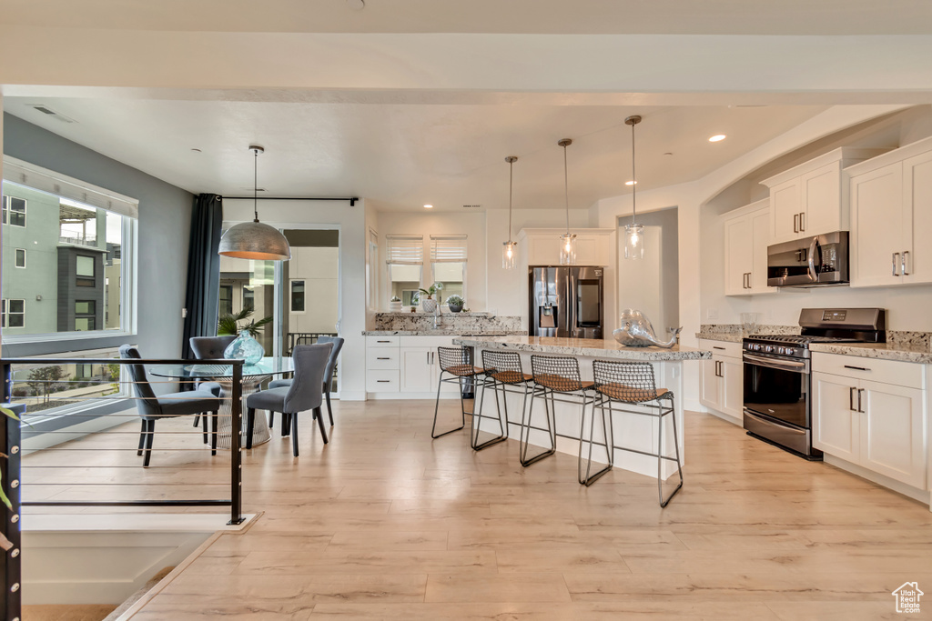 Kitchen featuring appliances with stainless steel finishes, a kitchen bar, white cabinets, a kitchen island, and recessed lighting