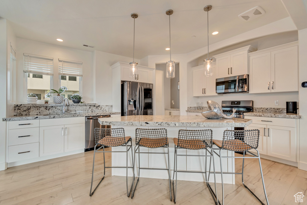 Kitchen with appliances with stainless steel finishes, a breakfast bar, white cabinetry, a sink, and a kitchen island