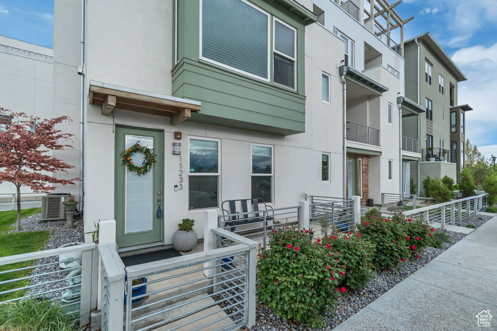 View of exterior entry with fence, stucco siding, and central air condition unit