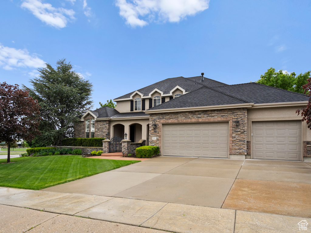 View of front of home with stone siding, a garage, stucco siding, a front yard, and concrete driveway