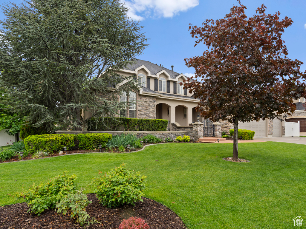 Traditional home with stone siding, driveway, a front yard, a garage, and stucco siding