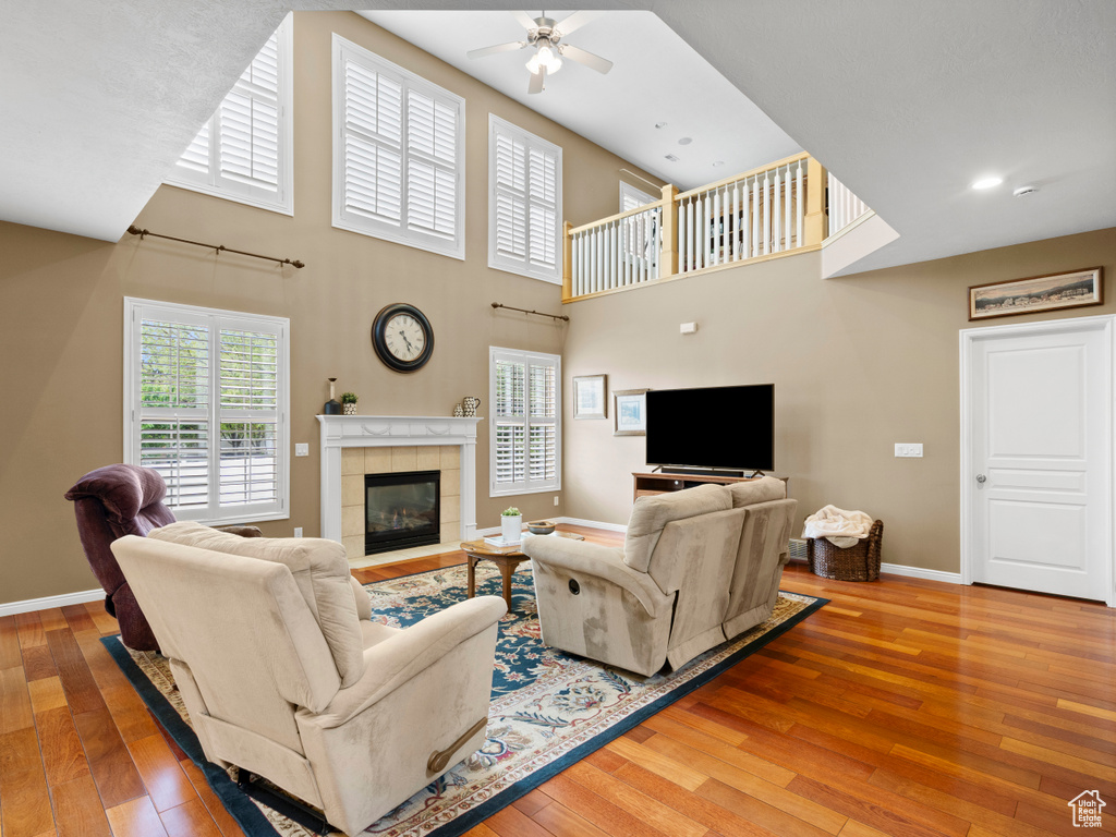 Living room featuring ceiling fan, hardwood / wood-style floors, baseboards, a fireplace, and a high ceiling