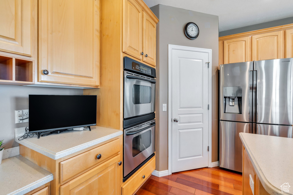 Kitchen featuring stainless steel fridge, light brown cabinetry, multiple ovens, light wood finished floors, and light countertops
