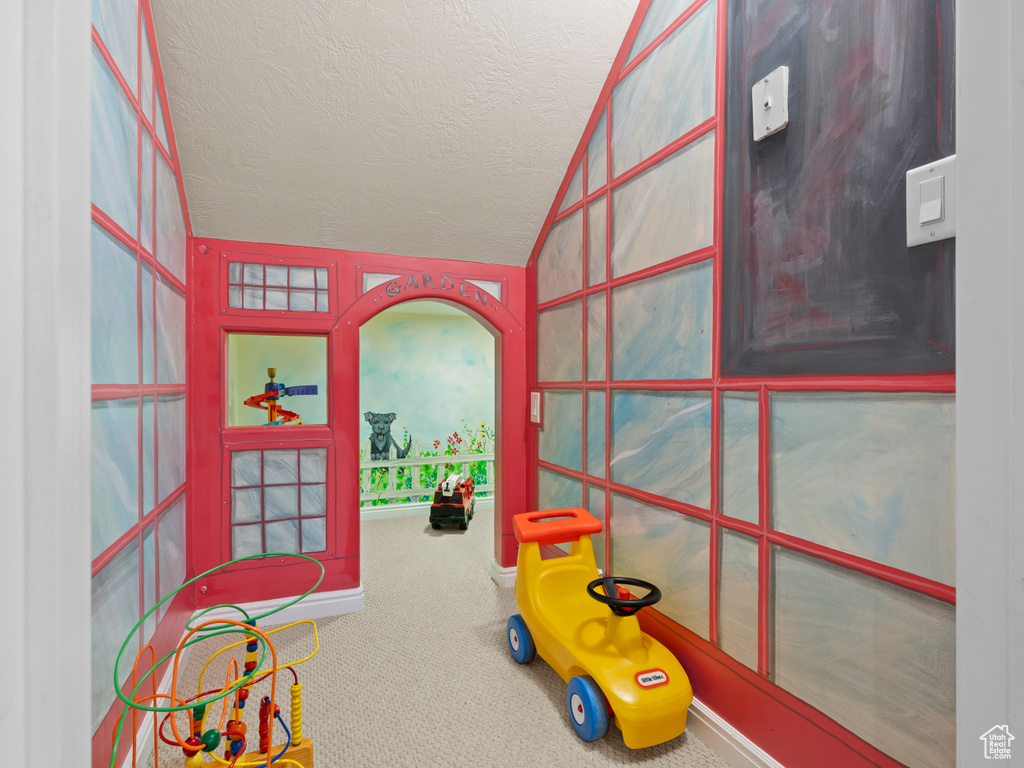 Recreation room featuring vaulted ceiling, carpet flooring, and a textured ceiling