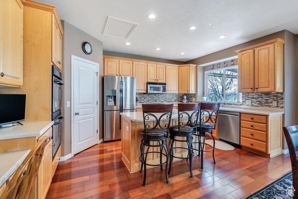 Kitchen with stainless steel appliances, light brown cabinetry, hardwood / wood-style floors, a kitchen breakfast bar, and recessed lighting
