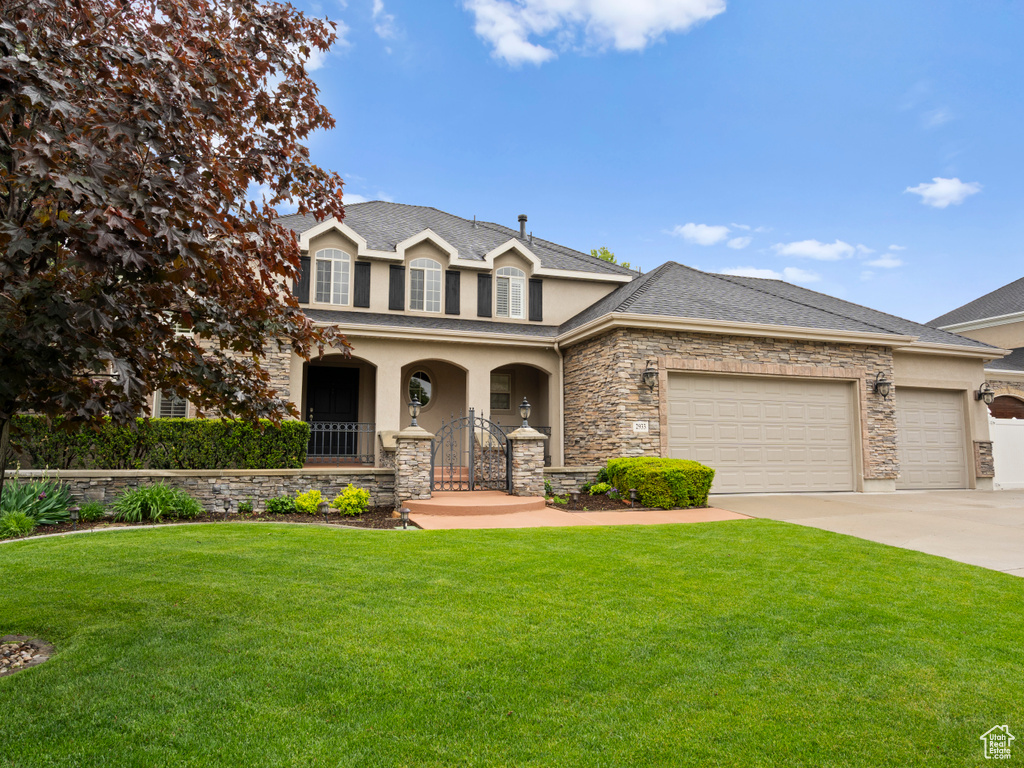 Traditional-style home with stucco siding, a front yard, an attached garage, driveway, and stone siding
