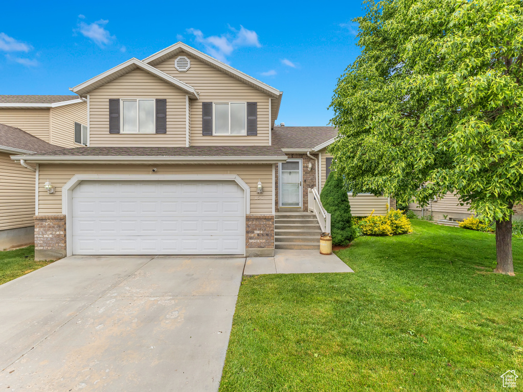 View of front of house featuring brick siding, an attached garage, a front yard, driveway, and roof with shingles