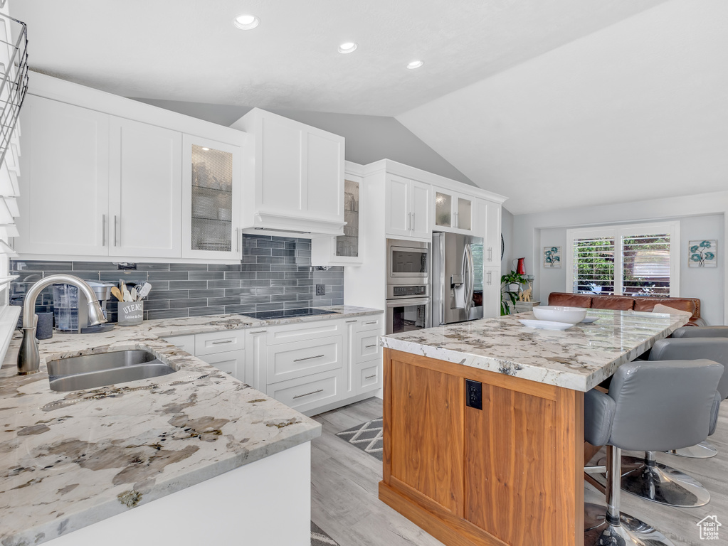 Kitchen featuring appliances with stainless steel finishes, a sink, vaulted ceiling, a center island, and a breakfast bar area