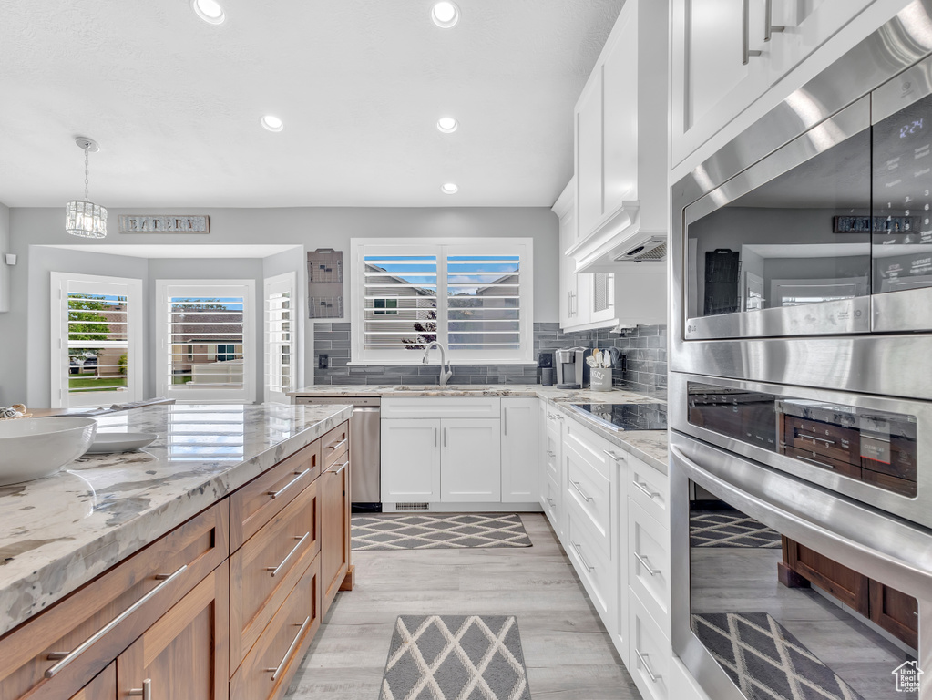 Kitchen featuring recessed lighting, light wood-type flooring, light stone countertops, decorative backsplash, and white cabinets