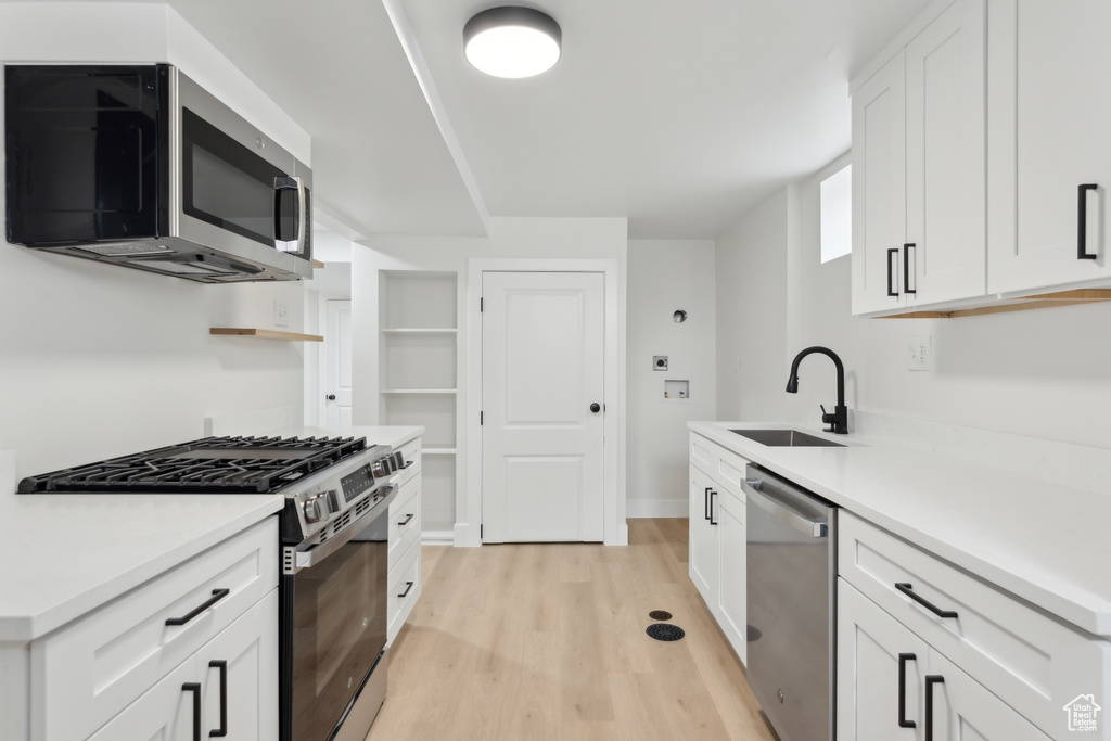 Kitchen featuring appliances with stainless steel finishes, a sink, light wood-style flooring, and white cabinets