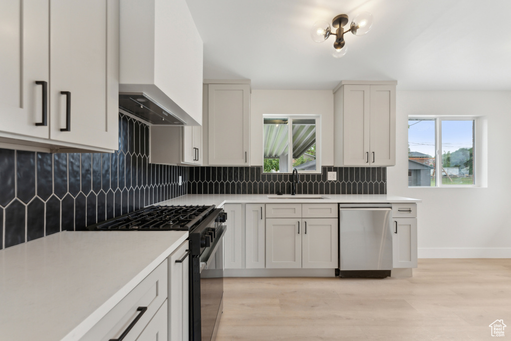 Kitchen featuring stainless steel dishwasher, black gas stove, a sink, wall chimney range hood, and light countertops