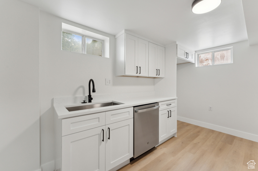 Kitchen with dishwasher, a sink, light wood-style floors, baseboards, and white cabinetry