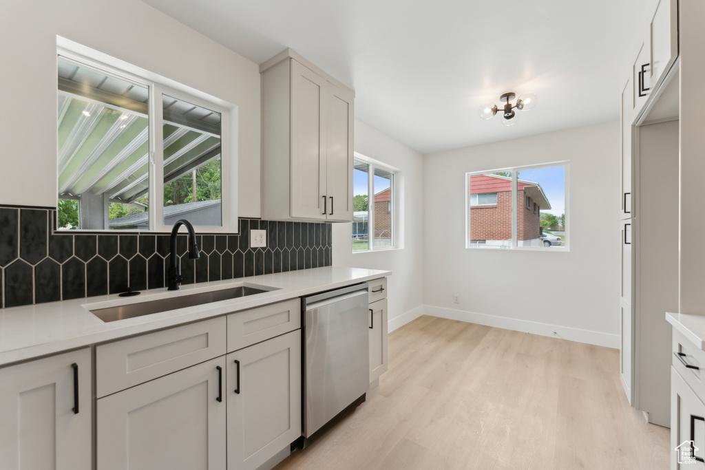 Kitchen with stainless steel dishwasher, a sink, light wood-style flooring, backsplash, and light countertops