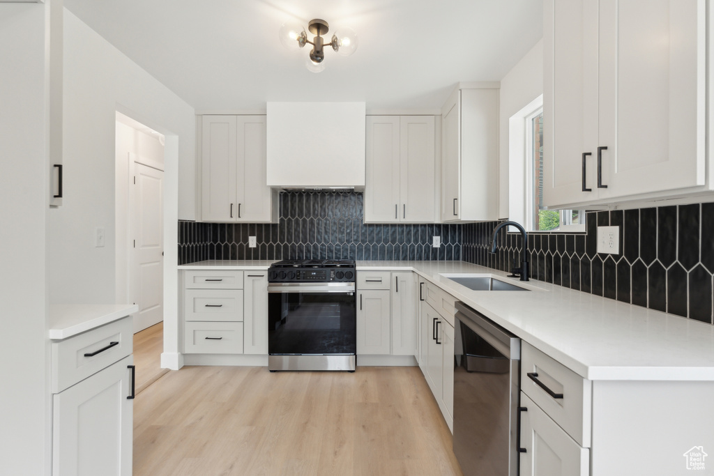 Kitchen with gas stove, stainless steel dishwasher, a sink, light wood-style flooring, and backsplash