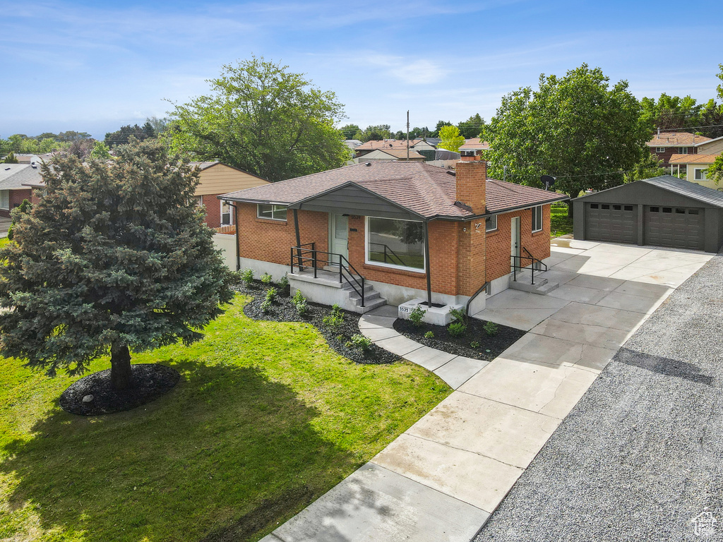 View of front facade featuring brick siding, an outdoor structure, a garage, a front yard, and a chimney