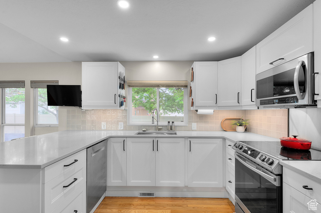 Kitchen featuring stainless steel appliances, a sink, a peninsula, light countertops, and white cabinets