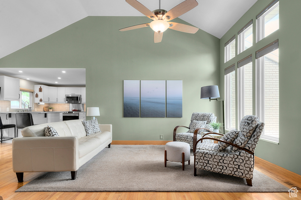 Living area with high vaulted ceiling, ceiling fan, light wood-style floors, and baseboards