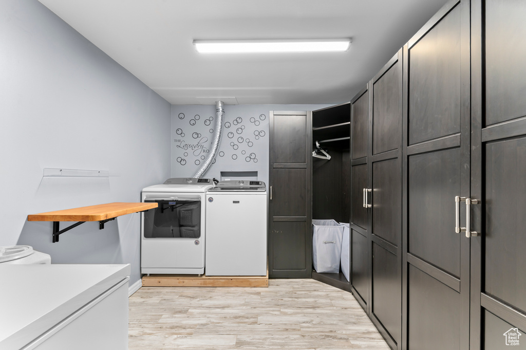 Laundry area with washing machine and dryer, cabinet space, and light wood-style flooring
