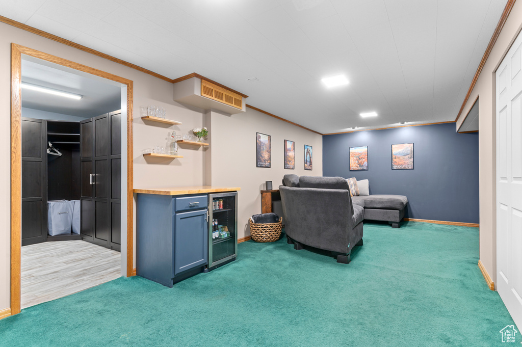 Carpeted living area with crown molding, baseboards, and wine cooler