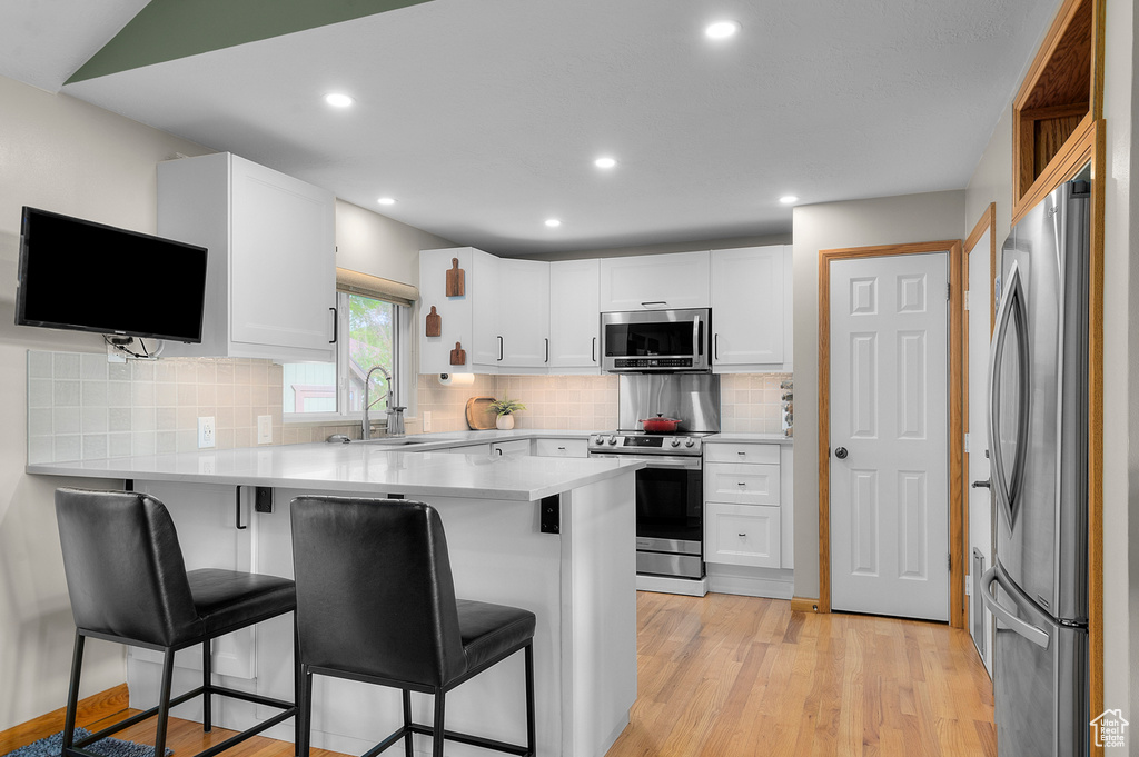 Kitchen with stainless steel appliances, a sink, a peninsula, a kitchen bar, and white cabinets