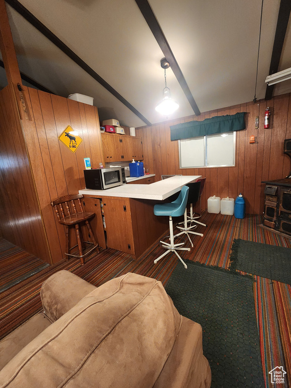 Kitchen with stainless steel microwave, wood walls, dark carpet, brown cabinetry, and an office area
